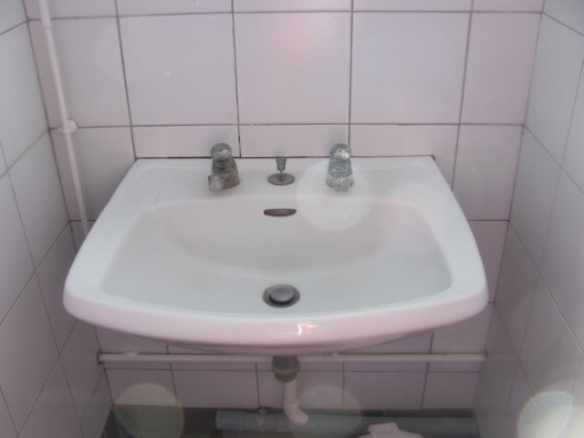 a single sink in a small white tiled cubicle