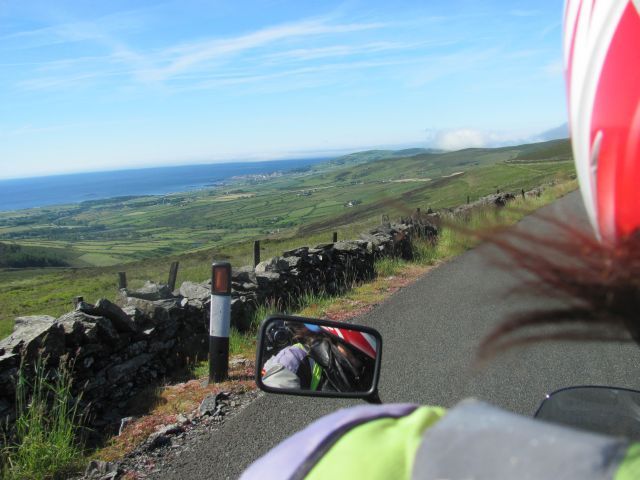 blue skies and the Manx coastline seen from the back of a motorcycle