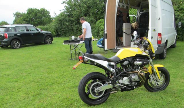 bright yellow buell motorcycle in front of a van and large gas barbeque