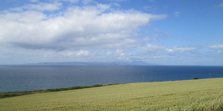 a crop filled field, then the sea and the isle of arran in the distance