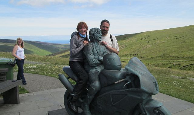 ren and sharon stand either side of joey dunlop's statue on the mountain part of the tt course