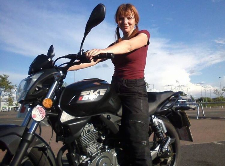 Sharon is sat on her 125 smiling in the sunshine