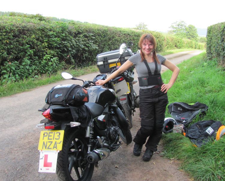 sharon stands by her bike with the new tyre fitted, smiling and posing