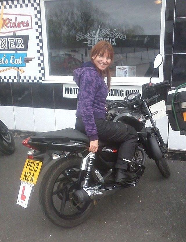 sharon sits on her 125 motorcycle looking over her shoulder and smiling