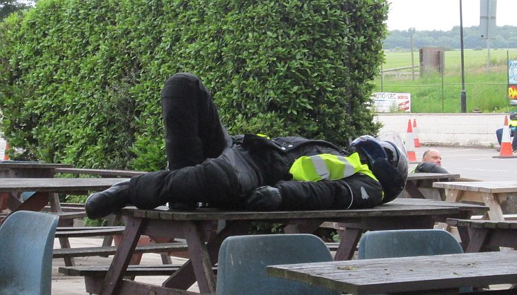 a motorcyclist lies on an outside table in all his motorcycle gear and helmet