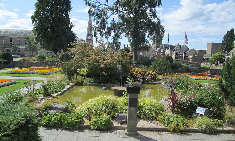 the sunken garden at forres. Flowers, trees, water feature and church in the background