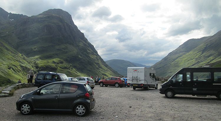 the vast valley of glencoe, and a gravel car park filled with cars, motorhomes and people