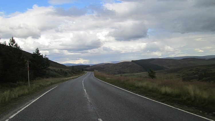 a road leading through green rolling hills and large hills in the distance, the cairngorms