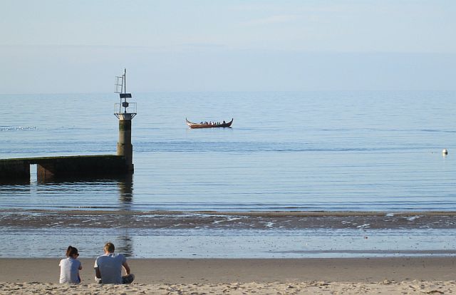 sun filled view across peel harbour beach with a viking style boat in the distanace