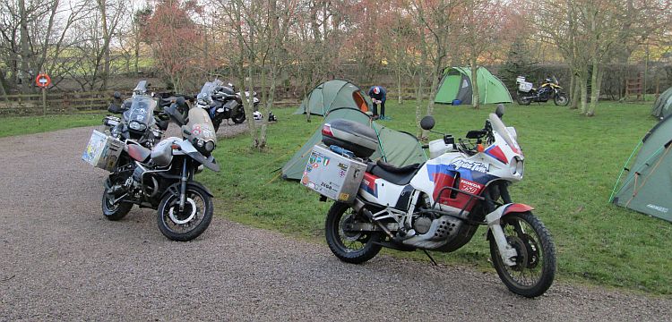 A variety of large adventure motorcycles and some tents at the takoda campsite
