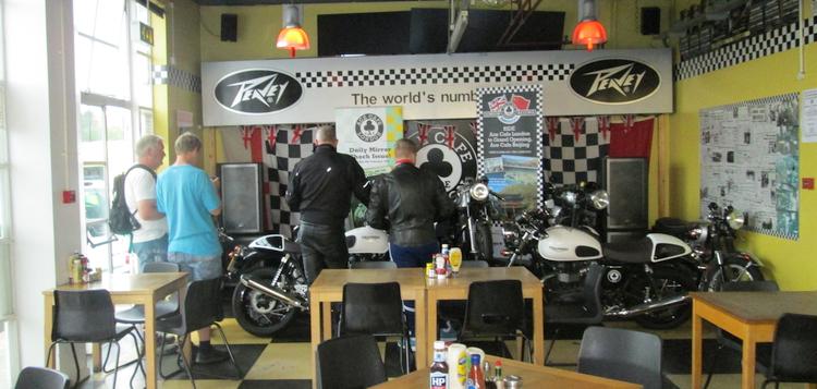 a few vintage motorcycles in a corner of the ace cafe with people looking at them