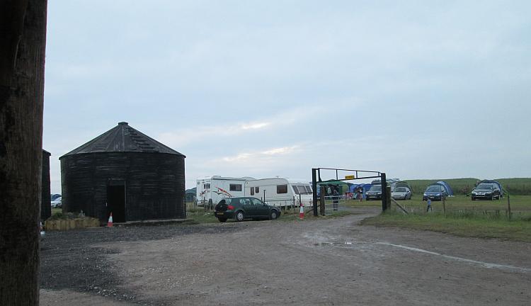 farm building and a muddy track into field filled with campers