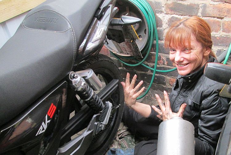 the gf holds her dirty hands up while tinkering with the chain on her motorbike