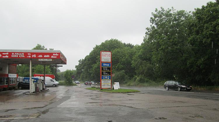 A rain soaked road and car with spray at a drab petrol station near hinckley