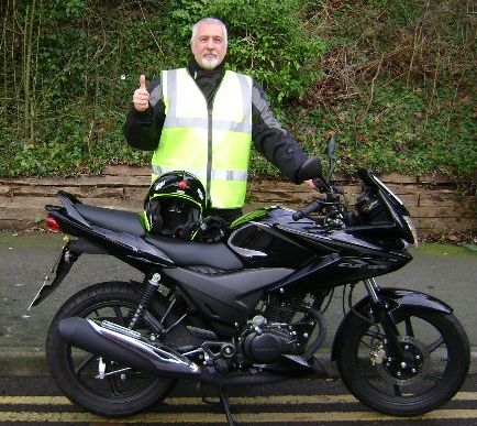 hugo stands next to his shiny black cbf 125 with a smile and thumbs up