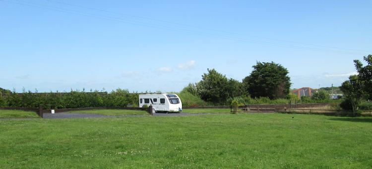 A solitary caravan on an empty green field at Llanfair Bach campsite, Holyhead
