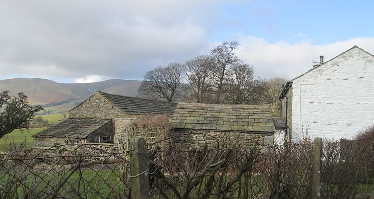 A scene across the hills of the dales with a stone built farm and farmyard in the foreground
