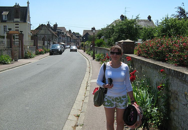 Sharon walks down a sun filled french street with her sunglasses on, smiling.