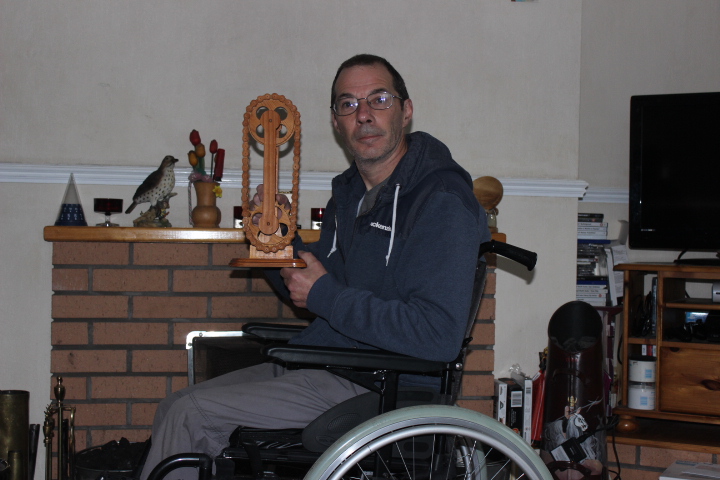 Tony holds a wooden chain/sprocket model while sat in his wheelchair
