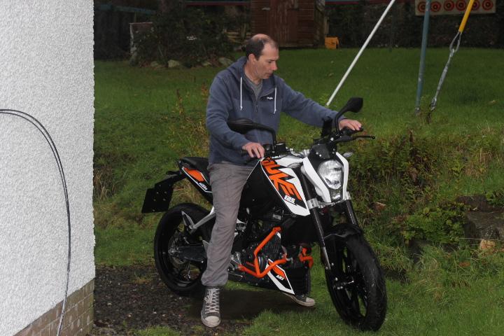 Tony stands astride the KTM 125 Duke, looking at the controls