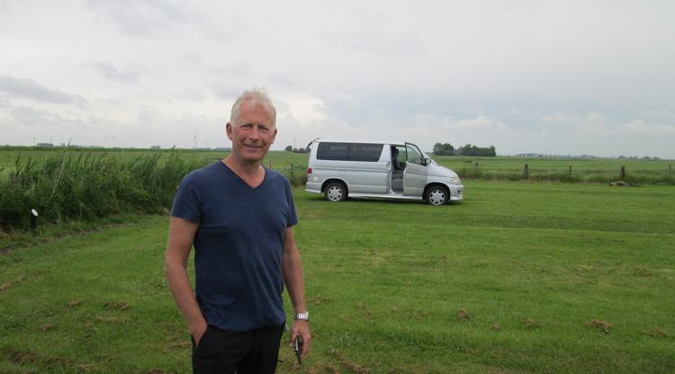 David stands in a camping field in front of his small campervan