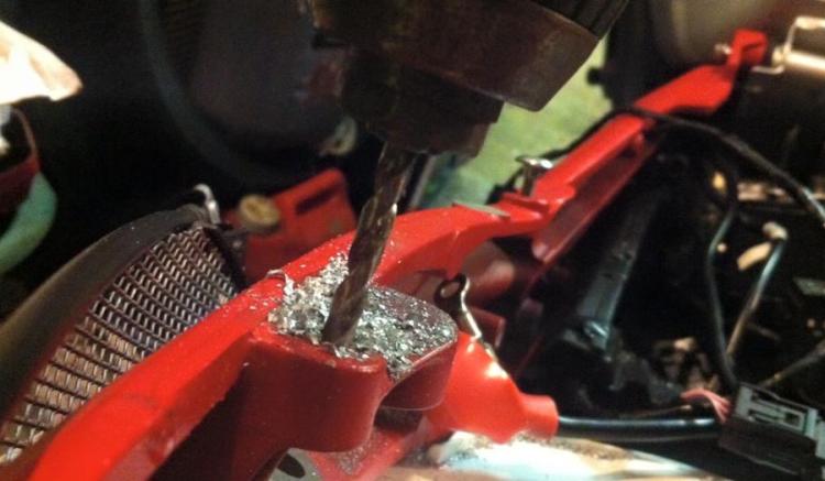 The drill bites into the bright red subframe to create the correct mounts for the brackets