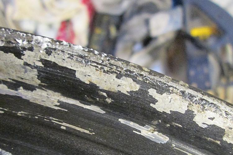 The wheel rim showing black paint flaking off the alloy walls.