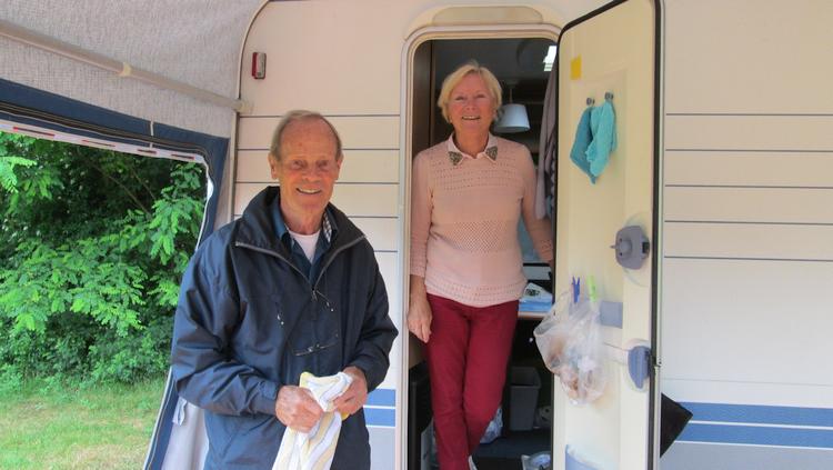 An aged couple smiling in the awning of their caravan