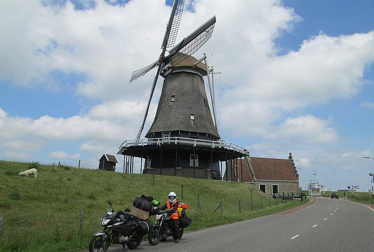 An old Dutch windmill with 2 motorcycles parked in front 