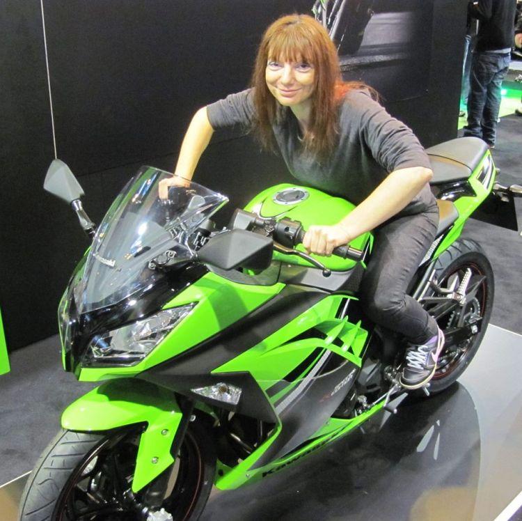 Sharon sits on a big green sporty Kawasaki at a motorcycle show