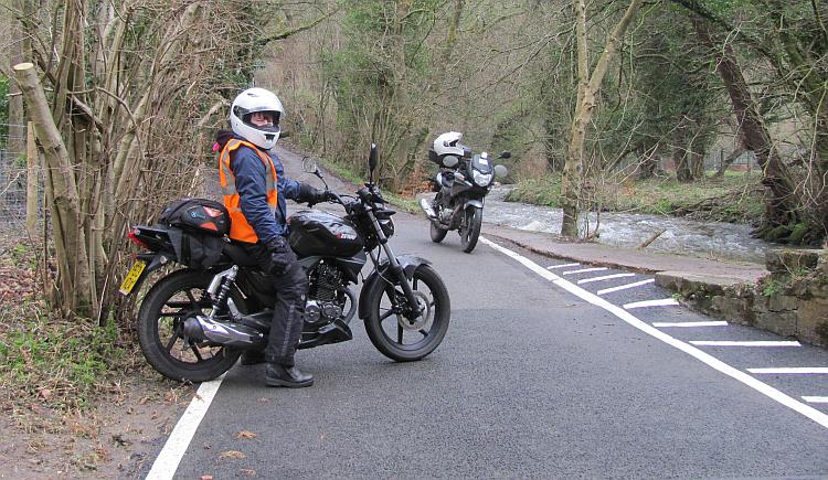 Sharon on her 125 down a narrow lane with a deep ford