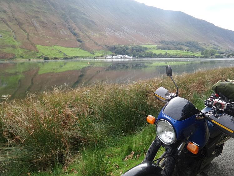 Looking across a broad lake to a steep mountainside with the bike in the front of the shot