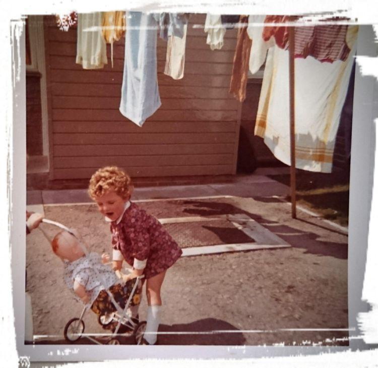 Toddler Sharon grabbing a toy pram in an old colour photo