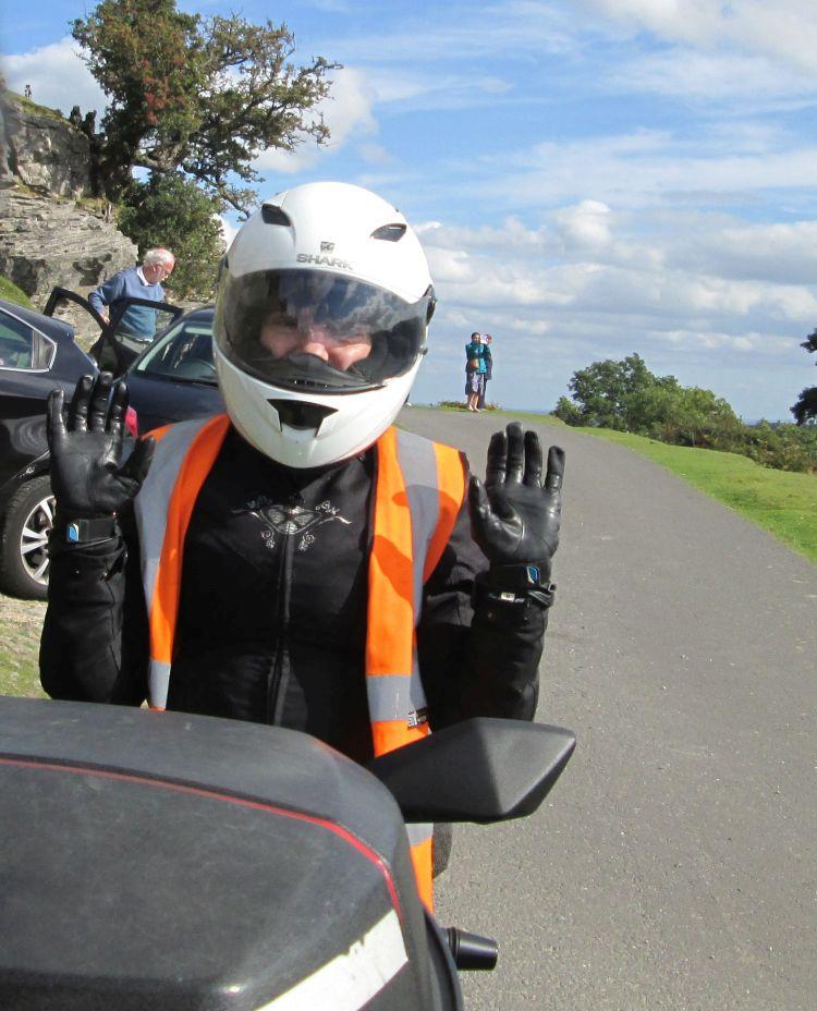 Sharon waves both hands at the camera with a big smile while still on the bike