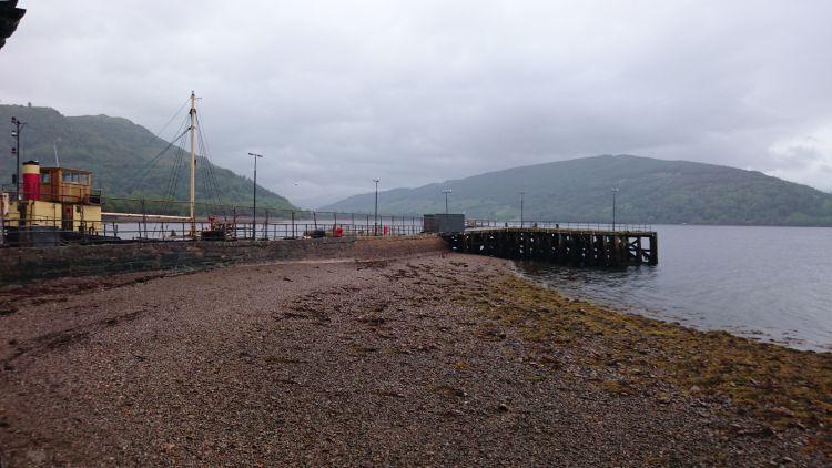 A wooden and stone jetty juts out into a misty Highland lock with a boat behind the wall