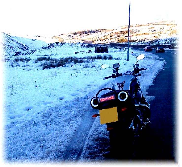 Tom's MT01 parked at the side of a lane passing through snowy hills and mountains