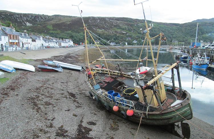 A boat on the shoreline, tha harbour and houses of Ullapool