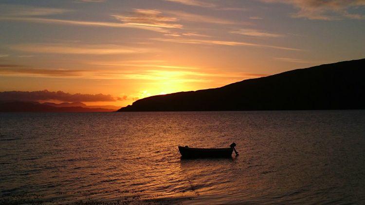 a small boat with outboard motor on the still waters near applecross as the sun sets deep orange