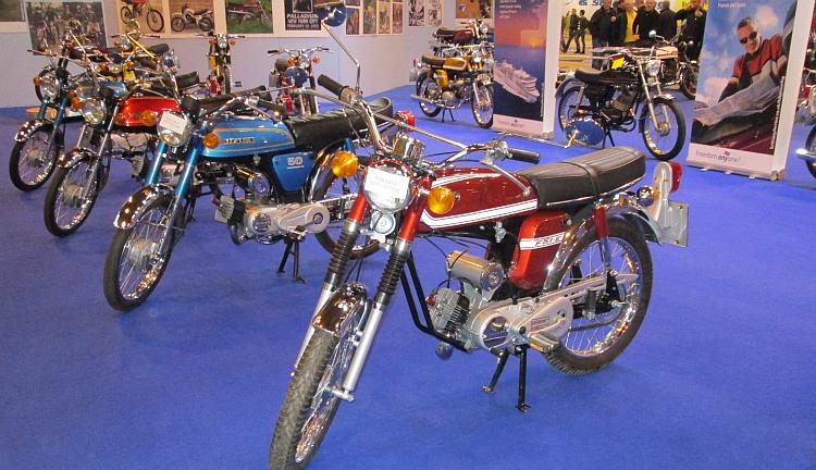 A selection of classic 50cc moped at a motorcycle show stand