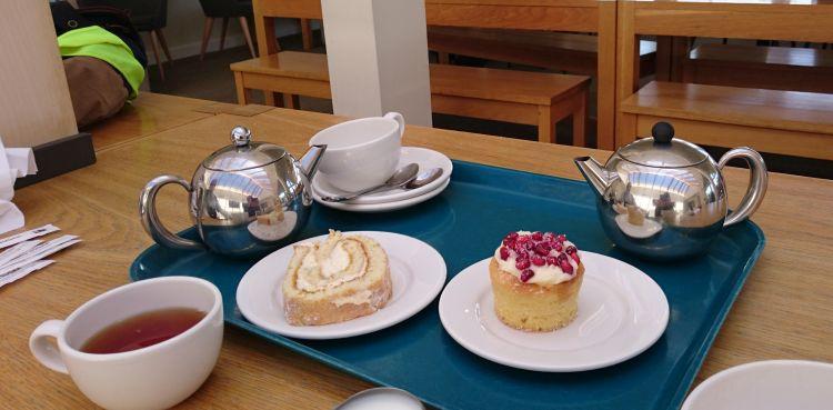 2 bright chrome tea pots, cups, saucers and sweet cakes on the table at Tebay services
