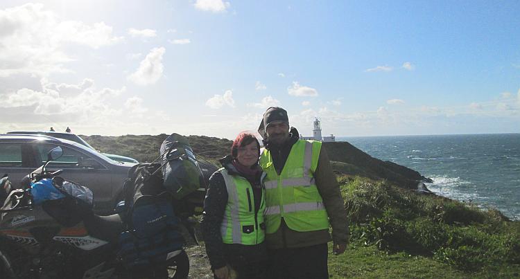 Ren and Sharon stand side by side in their bike gear with the lighthouse in the background