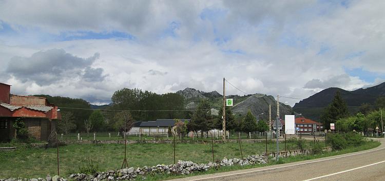 A few houses on the outskirts of a town along the road with the hills behind