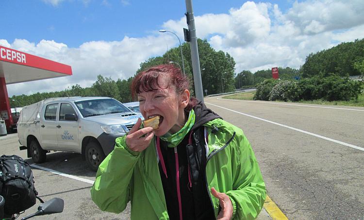 At another petrol station Sharon eats a sweet pastry in blue skies with some light cloud