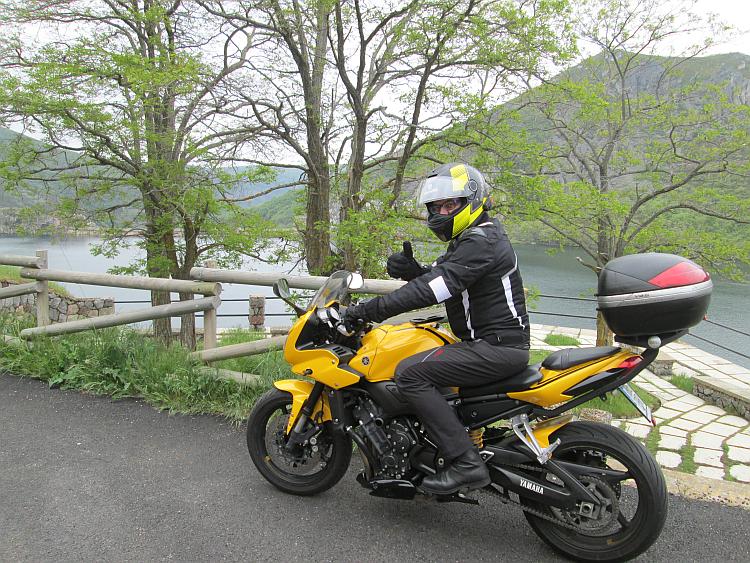 A biker on a large yellow motorcycle gives the thumbs up to the camera