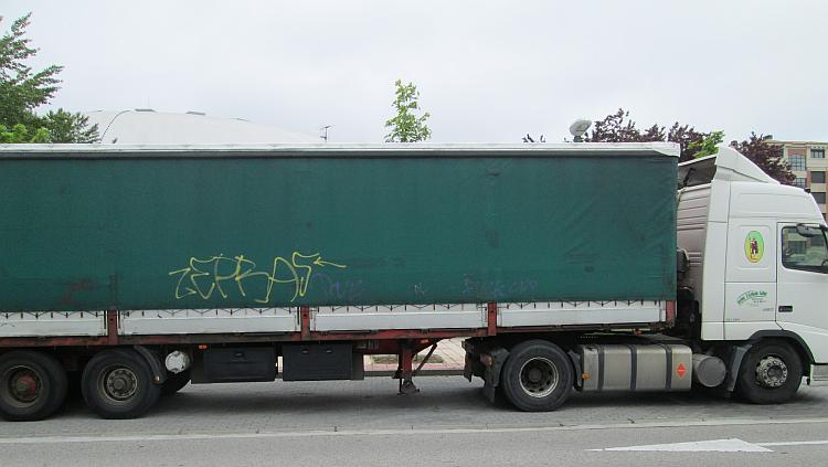 The curtain side of a large lorry has some graffiti sprayed on it