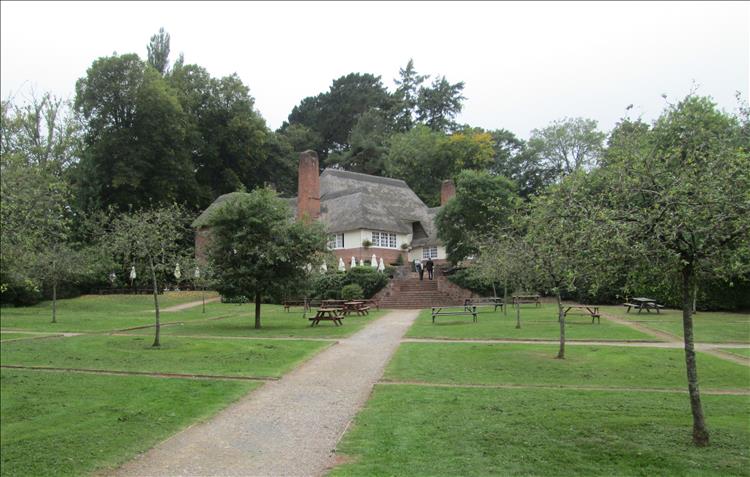 A large grass and tree filled garden with a large hall set in it all