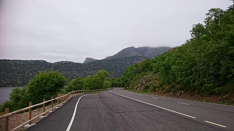 A road winds it's way alongside the reservoir amidst hills and valleys covered in trees and scrub