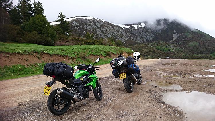 The 2 bikes loaded with camping gear on top of a mountain with some snow in the background