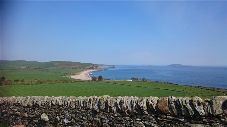 Carskey Bay, down below in the distance we see a sandy beach and lush green farmland