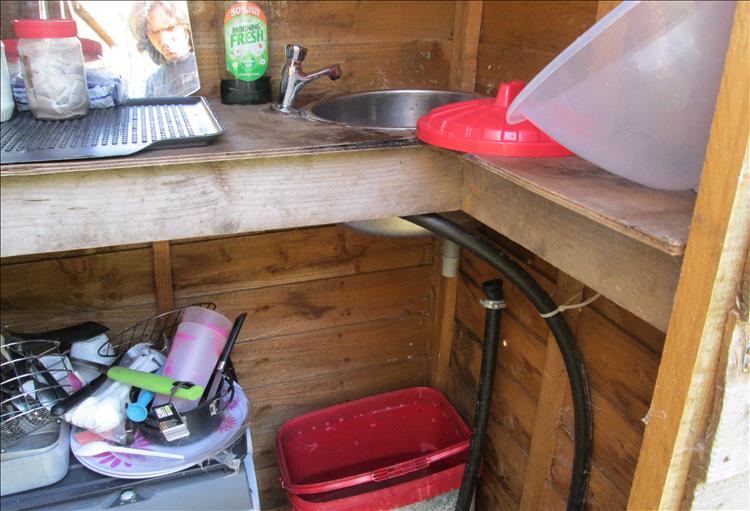 A questionable sink drains into a bucket in the tiny scruffy shed called the kitchen